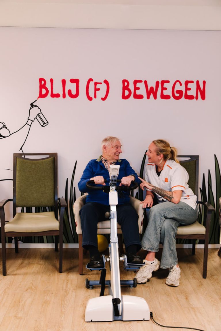 Bewoner zit op een stoel en praat samen met de verzorgster over een gezonde leefstijl
